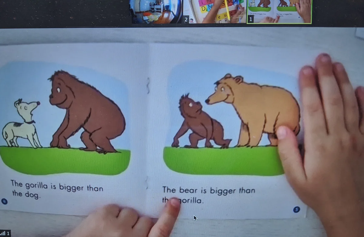A screen view of an online reading session showing a child pointing at text in a children's book with animal illustrations.