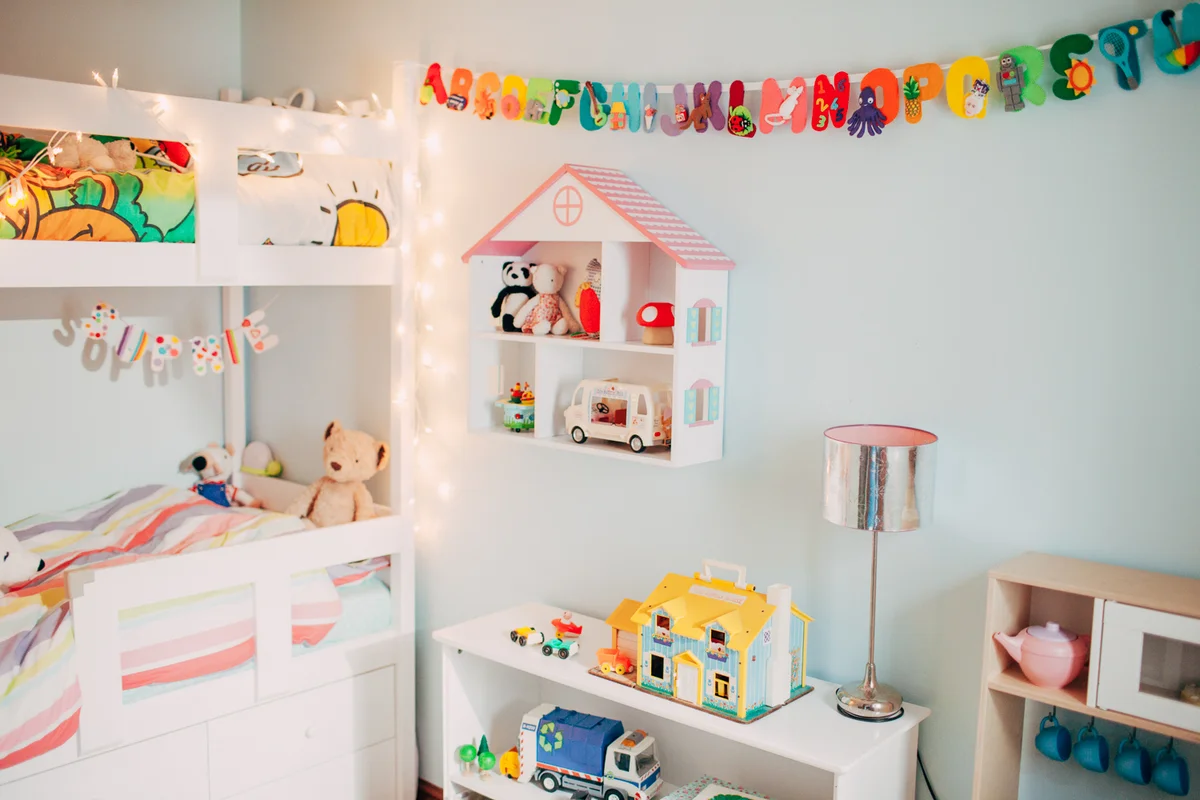A bright, organised playroom featuring wooden toys, dollhouses, and a colourful felt alphabet garland on a light blue wall