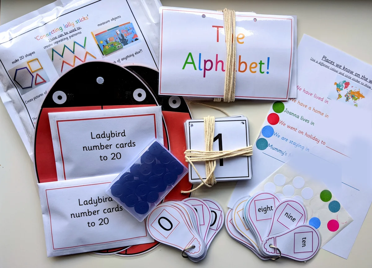 A collection of educational learning resources laid out before posting, including alphabet and number flashcards, ladybird maths cards, a tub of buttons, and activity sheets.