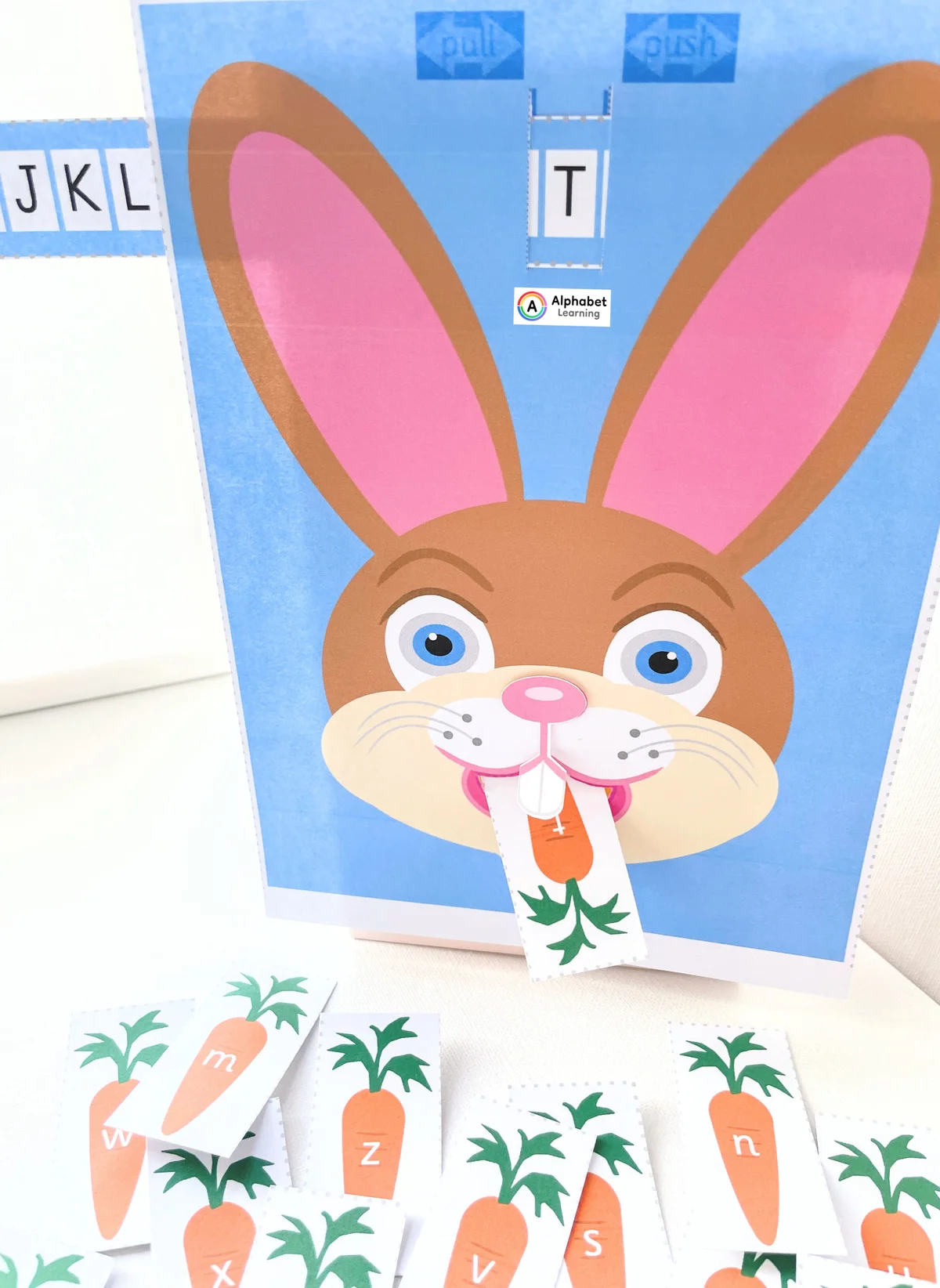 Interactive rabbit alphabet game featuring a rabbit face receiving a carrot card marked with the letter t into its mouth.